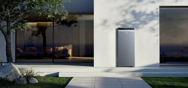 An Anker home battery unit mounted on the exterior wall of a modern house at dusk