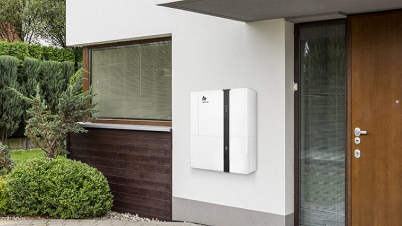A white home battery storage unit mounted on the exterior wall of a modern house next to the front door