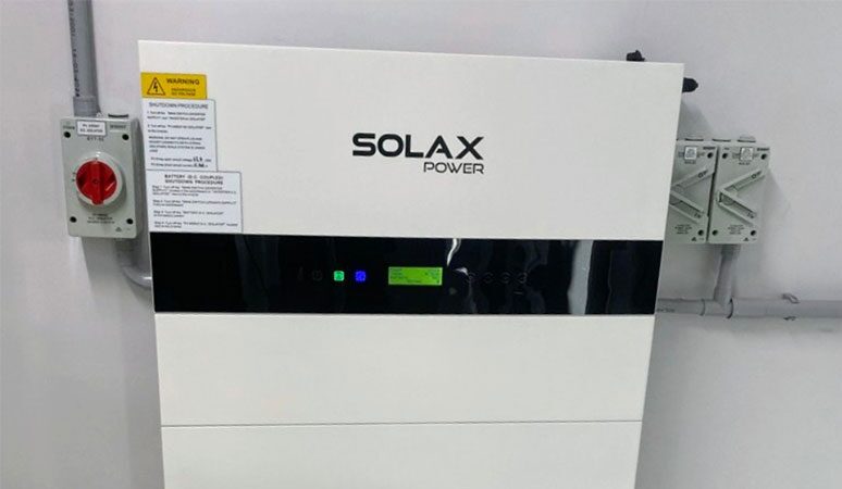 A white SolaX Power wall-mounted home battery storage unit installed on a wall next to electrical isolator switches