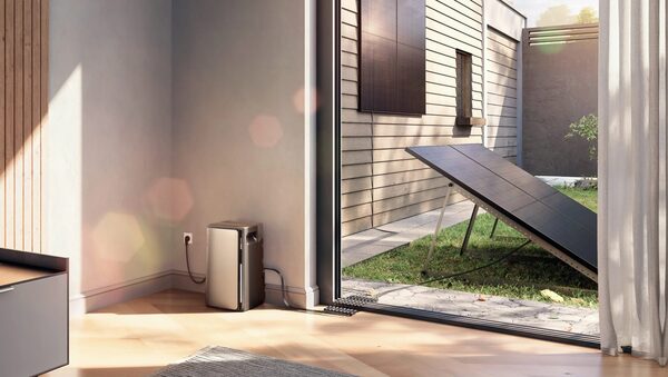 An EcoFlow home battery unit plugged in indoors next to a patio door, with solar panels on the lawn and wall outside