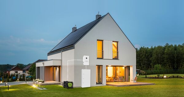 A Growatt home battery storage unit and inverter mounted on the exterior wall of a modern house with rooftop solar panels at dusk