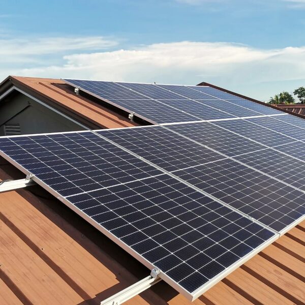 Solar panels mounted on a corrugated metal roof of a house under a blue sky