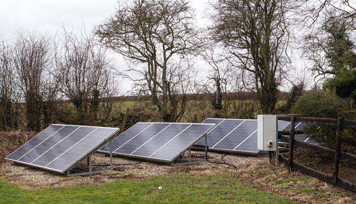 Ground-mounted solar panels in a rural garden next to a wooden fence and an electrical enclosure