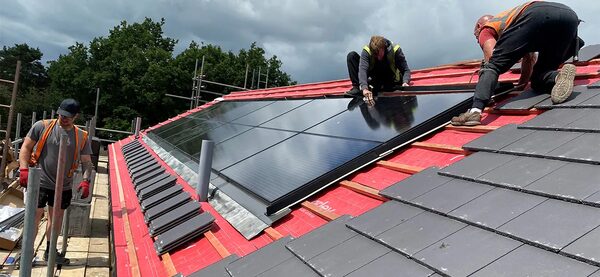 Roofers installing Marley solar panels on a house roof under construction with battens, membrane and grey tiles