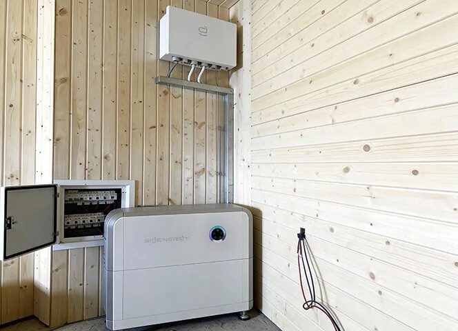 A Sigenergy home battery unit and wall-mounted inverter installed in a timber-clad utility room next to an open fuse box