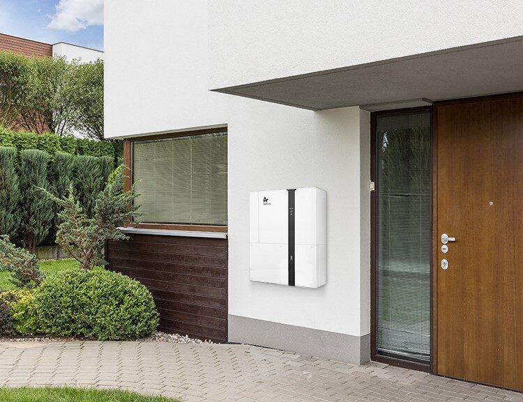 A white home battery storage unit mounted on the exterior wall of a modern house beside the front door