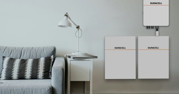 Duracell home battery units mounted on a living room wall next to a grey sofa and lamp