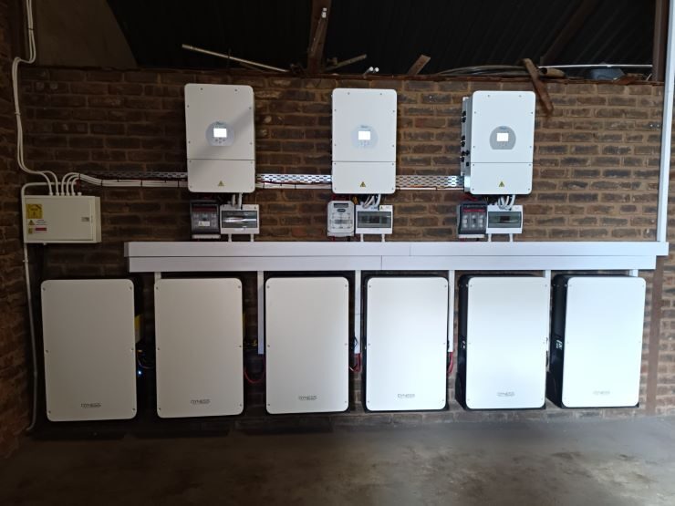 Six Dyness PowerBox Pro home battery storage units installed in a row on a brick wall beneath three wall-mounted inverters