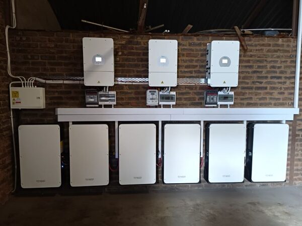 Six Dyness PowerBox Pro home battery storage units installed in a row on a brick wall beneath three wall-mounted inverters