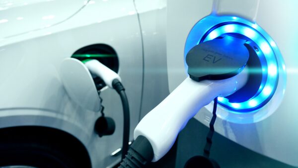 A white electric car being charged, with a charging plug in the socket surrounded by a glowing blue light ring