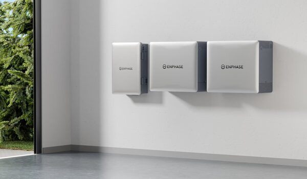 Three white Enphase home battery storage units mounted on an interior wall next to a window