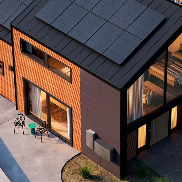 A modern timber-clad house with rooftop solar panels and Enphase battery units mounted on the exterior wall
