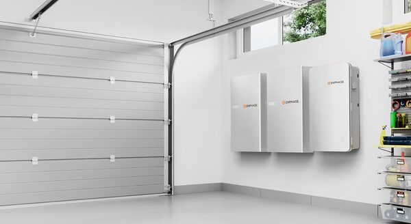 Three white Enphase home battery units mounted on a garage wall next to a sectional garage door