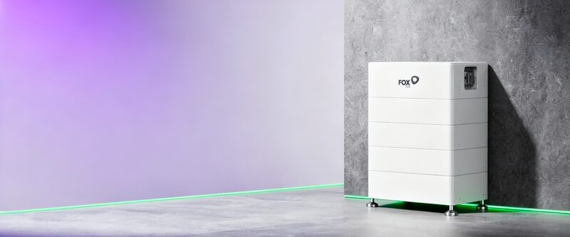 A white Fox ESS stacked home battery unit standing on the floor against a grey concrete wall with purple and green studio lighting