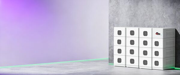 A stack of white Fox ESS high-voltage battery storage modules arranged in a grid against a concrete wall in a studio setting