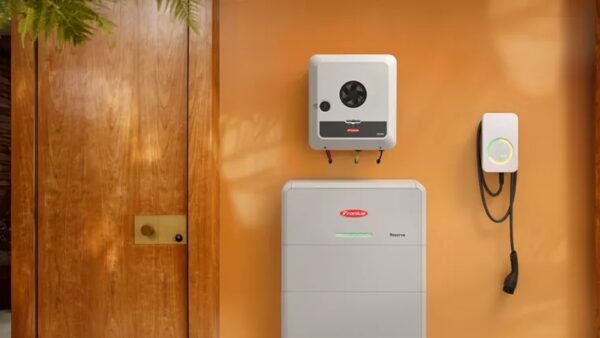 A Fronius GEN24 inverter and Fronius Reserva battery mounted on an orange wall next to an EV charger