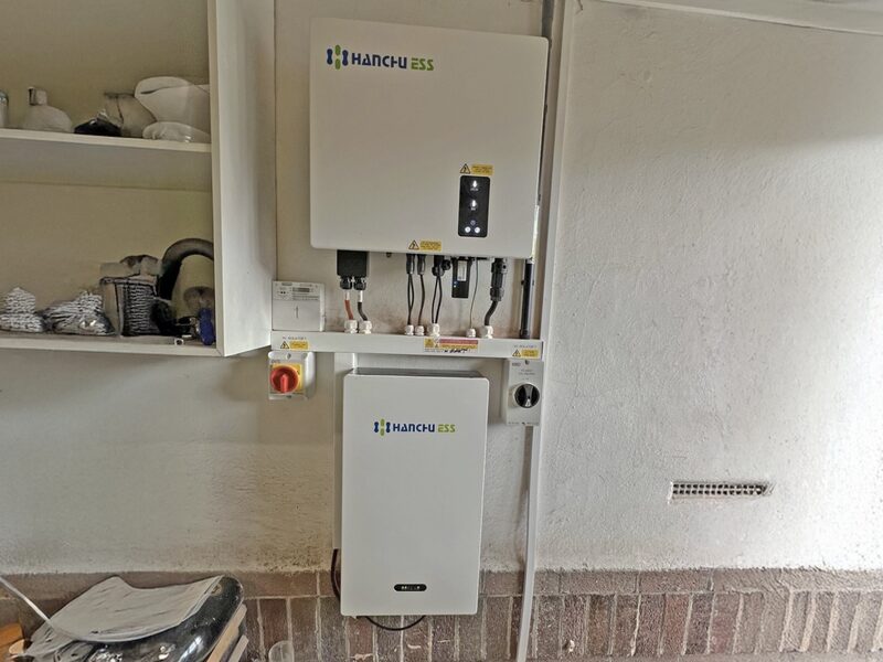 A Hanchu ESS home battery and inverter unit installed on a garage wall with visible wiring and an isolation switch