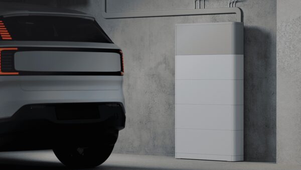 A white home battery storage unit mounted on a concrete garage wall next to a parked electric car