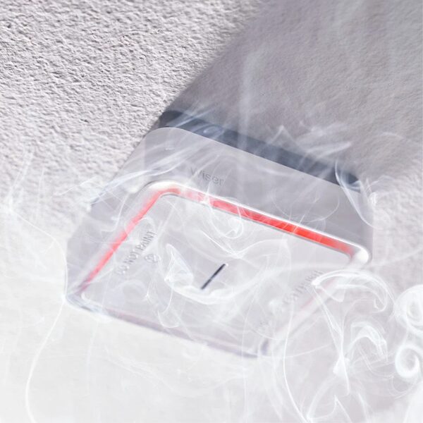 A Wiser ceiling-mounted smoke and heat alarm with a red warning glow, surrounded by smoke