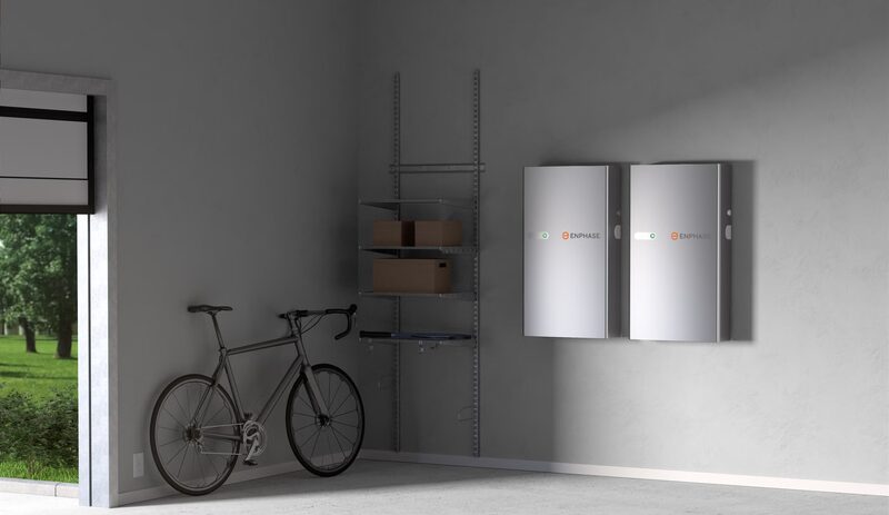 Two Enphase IQ home battery units mounted on a grey garage wall next to a bicycle and shelving