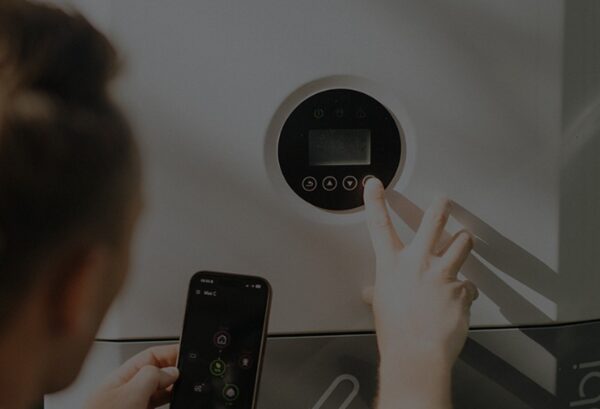 A person pressing buttons on the control panel of a myenergi libbi home battery while holding a smartphone showing the app