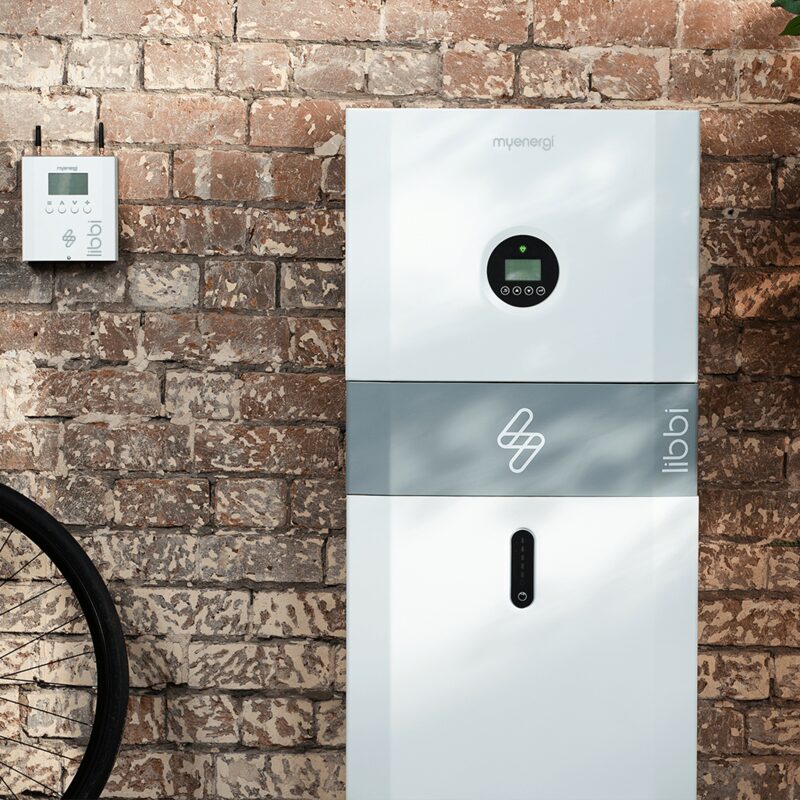 A white myenergi libbi home battery storage unit mounted against a brick wall with a small controller box beside it
