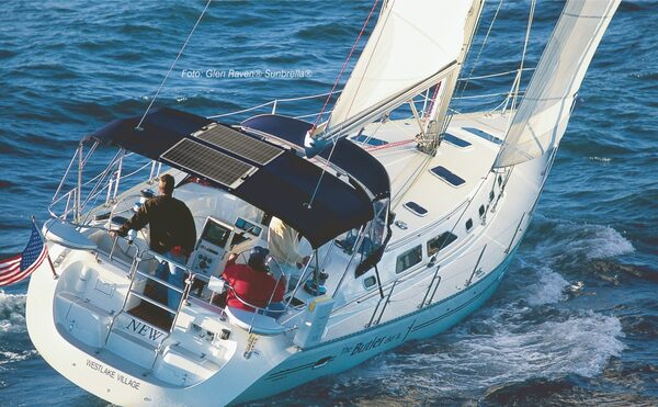 A sailing yacht with flexible solar panels mounted on its navy bimini canopy out at sea