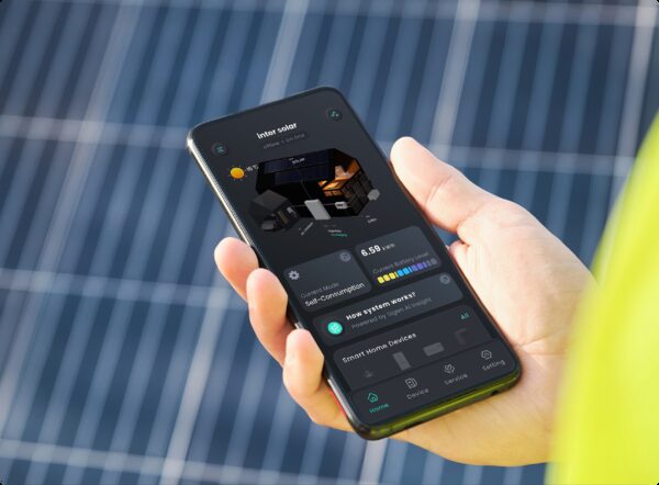 A hand holding a smartphone showing a solar energy monitoring app in front of solar panels