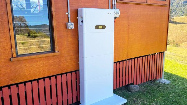 A white SOFAR stacked home battery unit installed on the outside wall of a wooden house