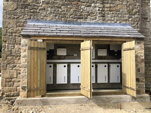 SolarEdge battery storage units and inverters installed in a timber-doored enclosure on a stone building exterior