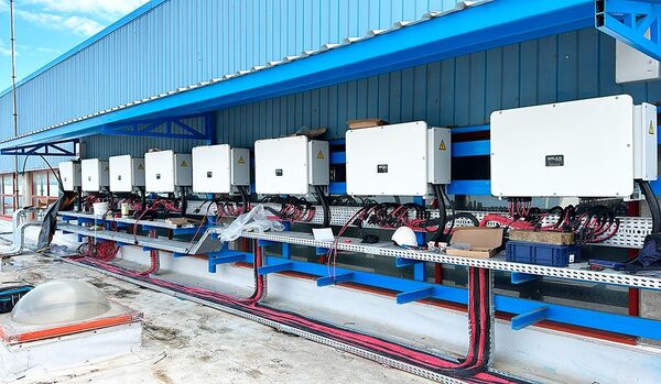 A row of white SolaX solar inverters mounted on a blue steel frame on a commercial rooftop with red cabling