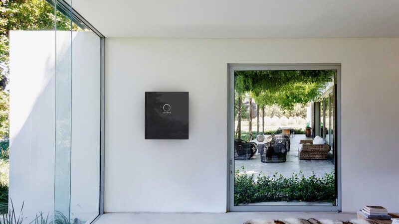 A black wall-mounted home battery unit installed on a white wall in a modern house interior