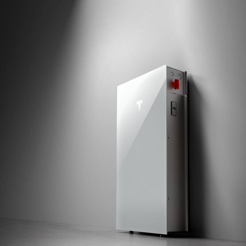 A white Tesla Powerwall home battery unit mounted against a plain grey wall