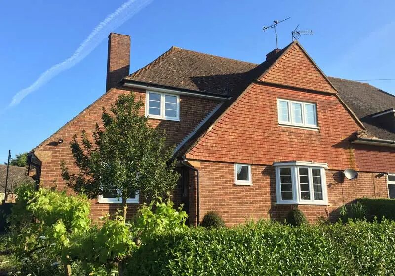 A 1950s brick semi-detached house with tiled roof and white windows under a blue sky