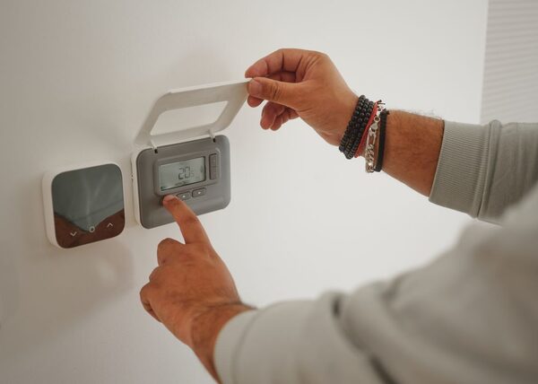 A person adjusting a wall-mounted digital thermostat next to a smart thermostat control in a home