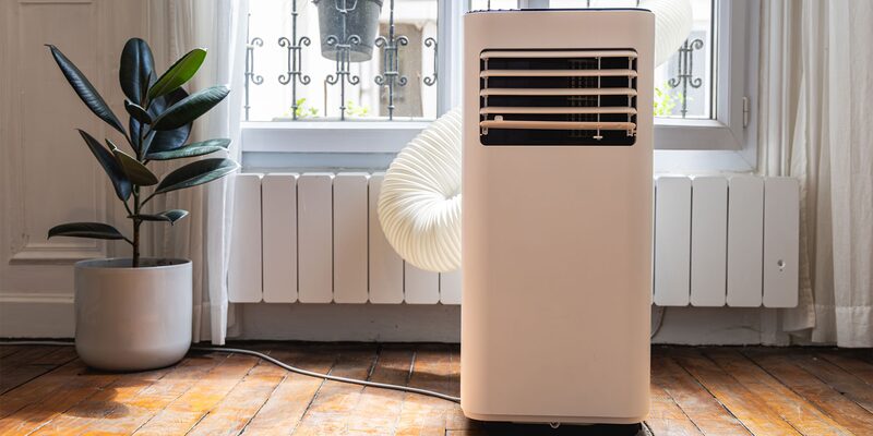 A portable air conditioner with an exhaust hose in a bright room next to a radiator and potted plant
