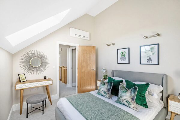 A wall-mounted white air source heat pump indoor unit installed high on the wall of a bright loft-conversion bedroom