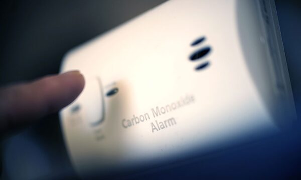 A finger about to press the test button on a white carbon monoxide alarm