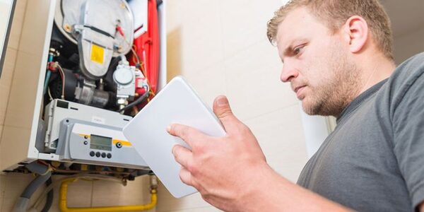 An engineer holding a tablet while inspecting the open internal workings of a wall-mounted gas boiler