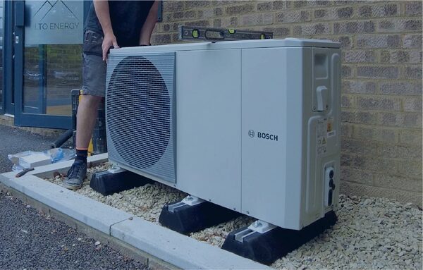An installer positioning a Bosch air source heat pump unit outside a brick building