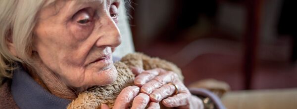 An elderly woman wrapped in a blanket, looking cold and frail indoors