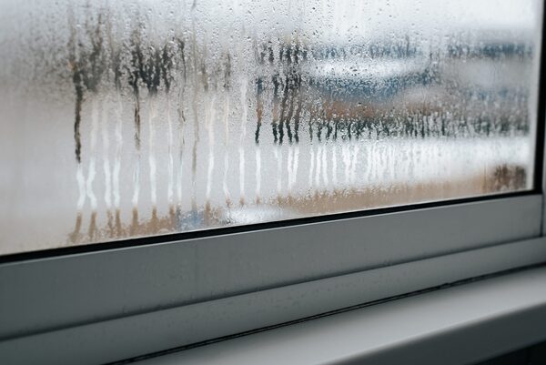 A double-glazed window with condensation running down the inside of the glass above a grey window sill