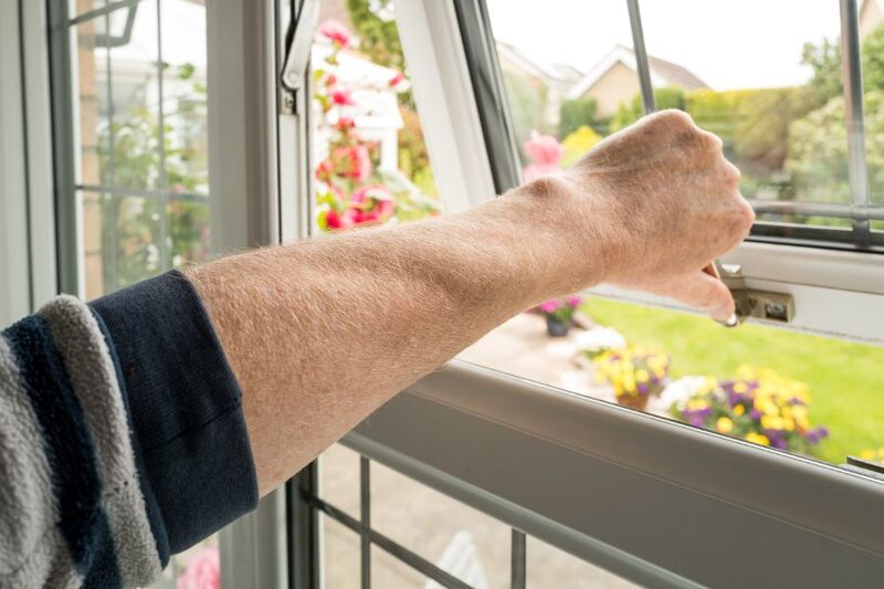 A person's arm opening the latch of a white uPVC double glazed window overlooking a garden