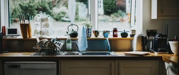 A domestic kitchen sink area with washing-up items, kettle and toaster on the worktop beneath a window