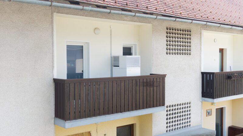 A white heat pump unit installed on the balcony of an apartment house