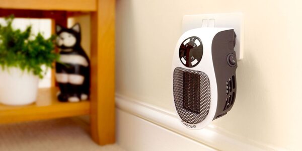 A small white and grey plug-in mini electric heater plugged into a wall socket near the skirting board