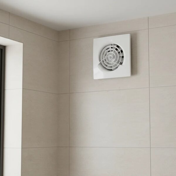 A white square extractor fan mounted high on a beige tiled bathroom wall