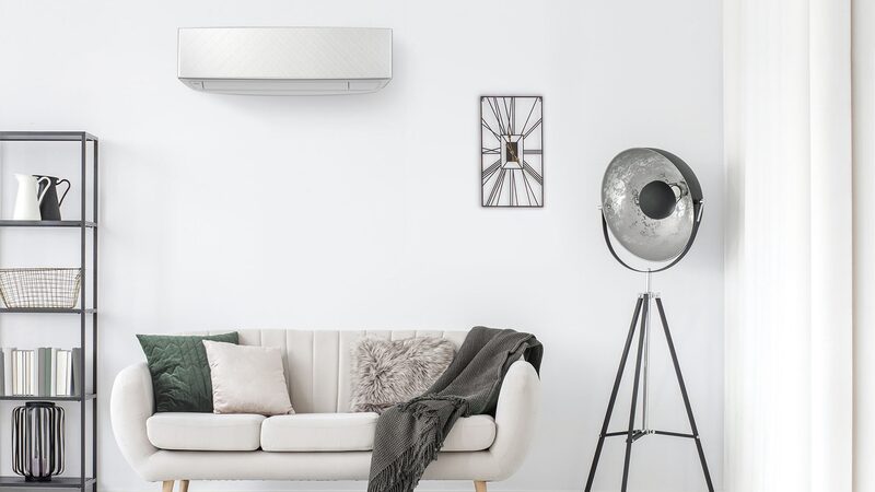 A white wall-mounted air conditioning heat pump unit installed above a sofa in a bright living room