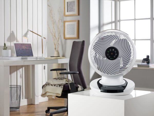 A white MeacoFan desk fan on a table in a bright home office with a desk, laptop and chair behind