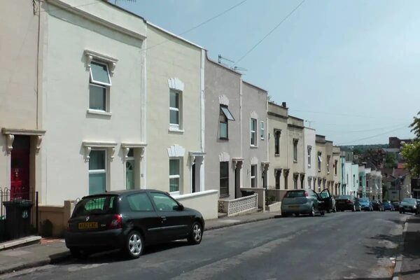 A street of UK terraced houses with parked cars along the road